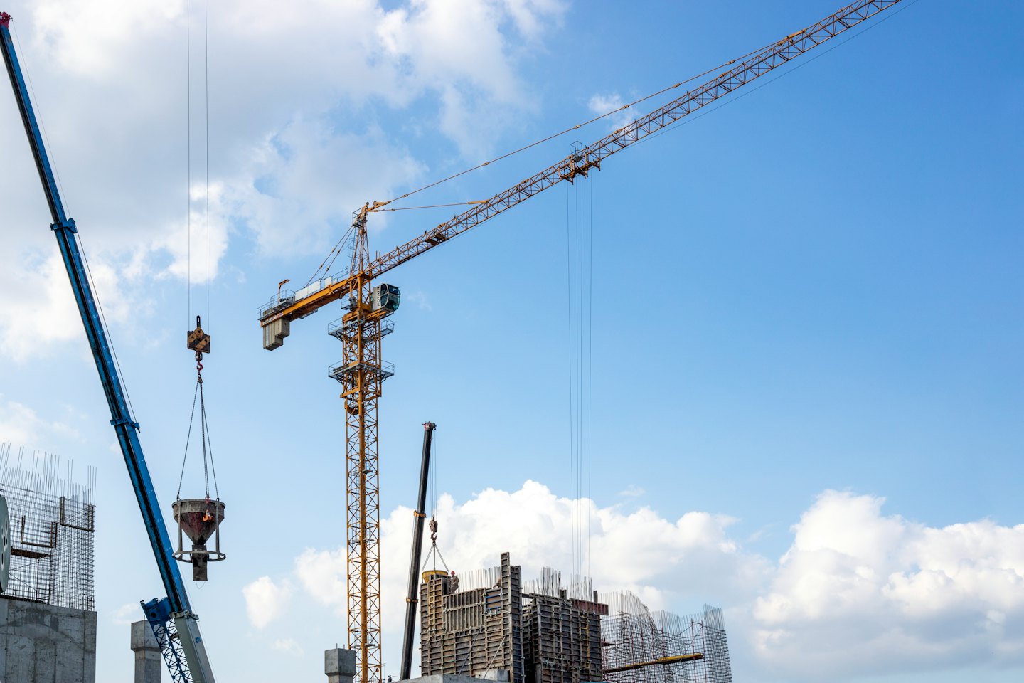 Dwa dźwigi budowlane podnoszące ciężkie materiały na placu budowy.